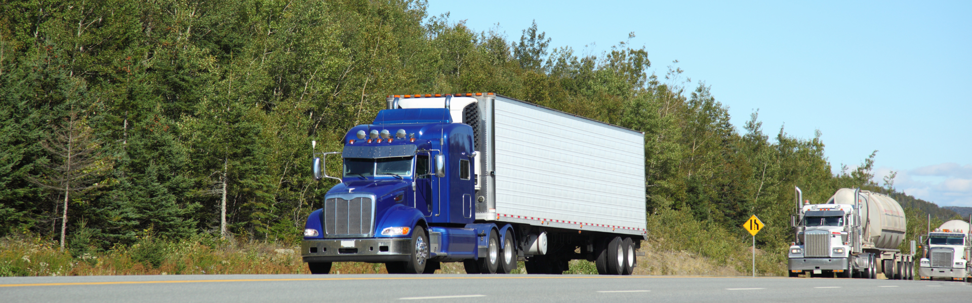 blue semi truck with white trailer on road with trees in the background