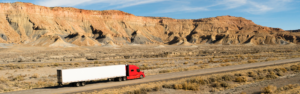 red semi truck pulling white trailer across a desert landscape