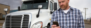 Man in flannel shirt looking at cell phone with white semi truck in background