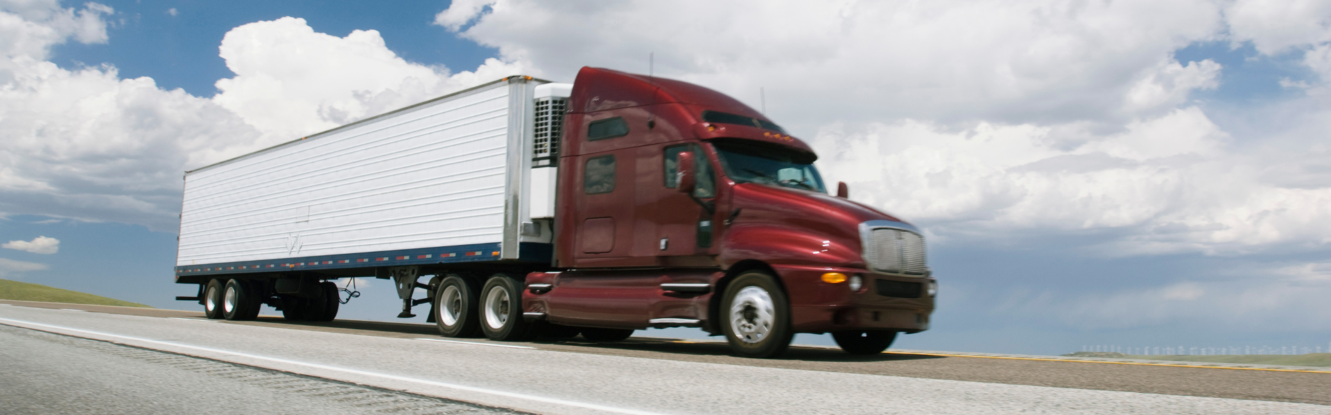 dark red semi truck with white trailer parked on road with partly cloudy sky in background