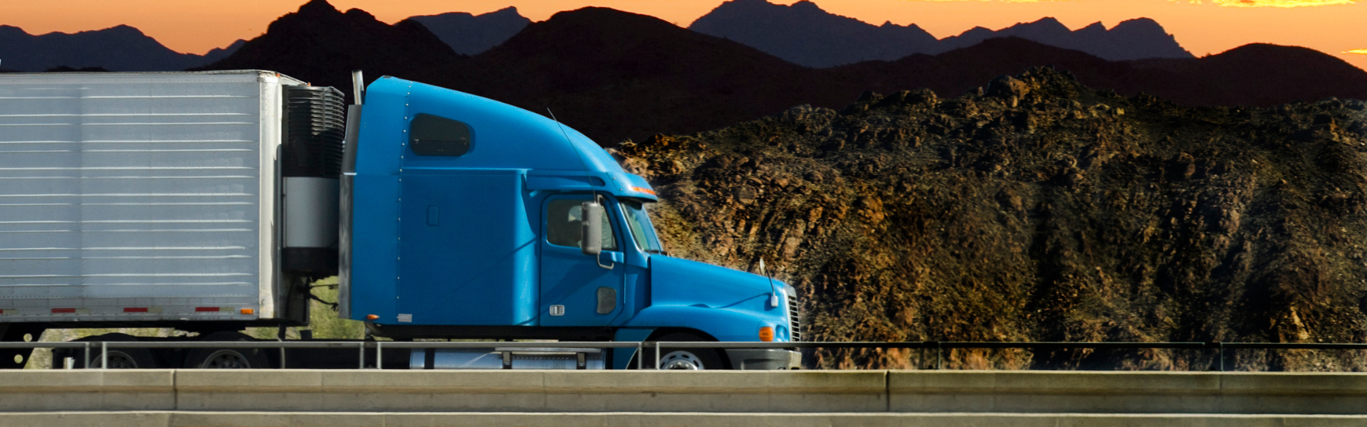 blue semi truck with white trailer on road with mountains and sunset in background