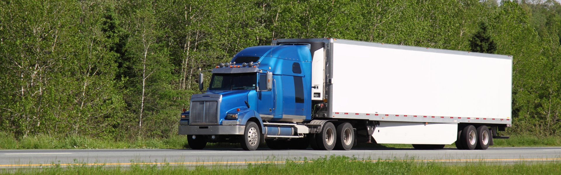 blue semi truck pulling white trailer on road with trees in background