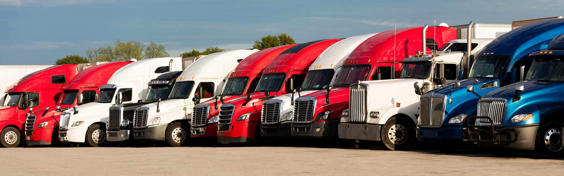Variety of semi trucks parked in a row in a parking lot designed for truck parking