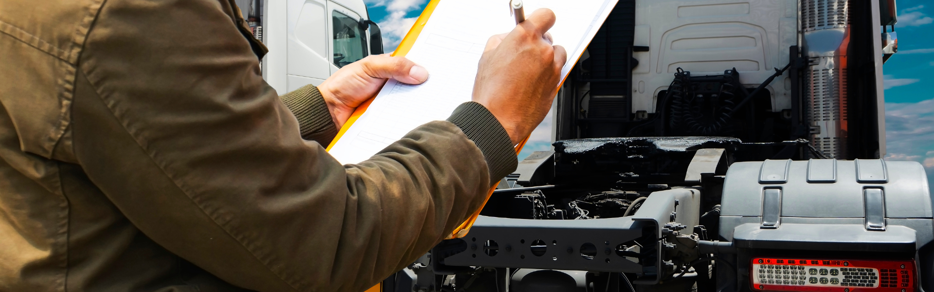 man with clipboard held up writing in pen with semi truck in background