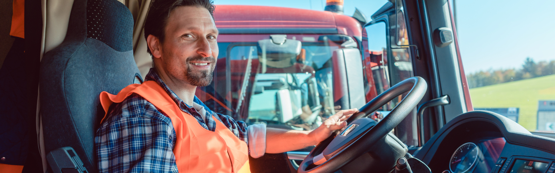 man wearing orange safety vest in cab of semi truck at steering wheel