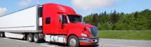 red semi truck with white trailer parked on roadside with green trees in the background.