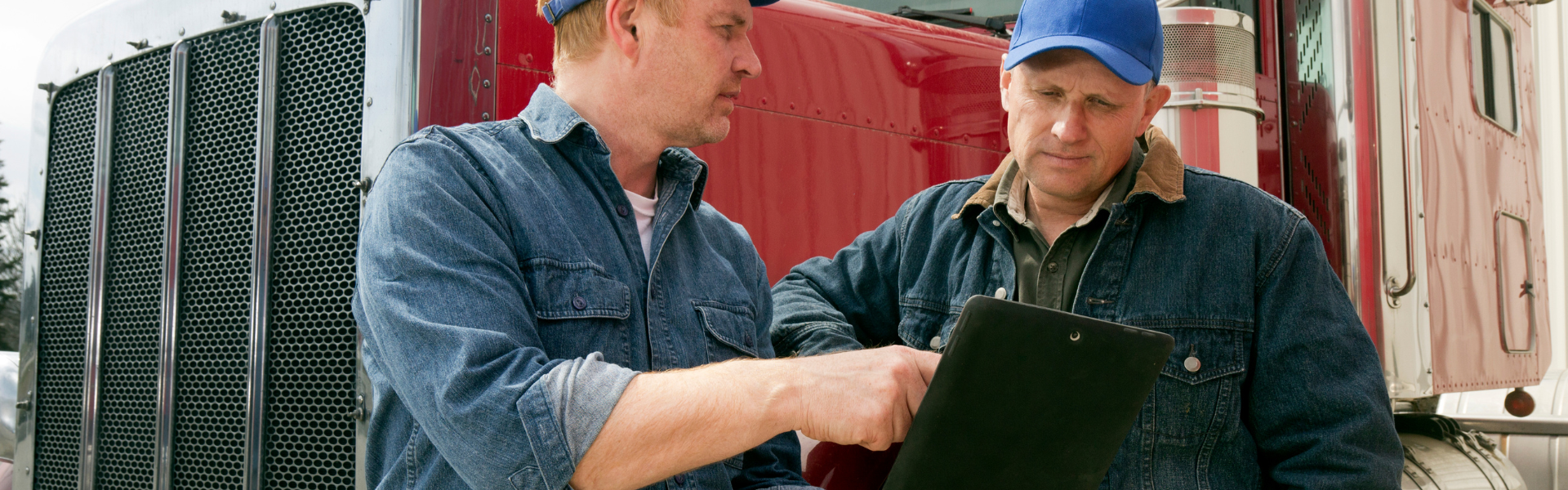 two men looking at clipboard with semi truck in background