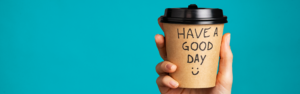 disposable coffee cup that reads "have a great day" being held up on blue background driver appreciation week