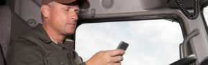 man in cab of semi truck at steering wheel looking at phone, truck parking, truck parking app, trucklots