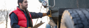 man in red vest holding clipboard standing next to semi truck, truck inspections, roadcheck