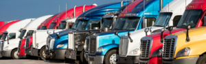 Variety of semi trucks in many different colors, makes, and years parked in a row.