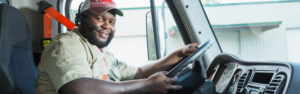 black man wearing ball cap in the cab at the wheel of semi truck