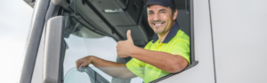 man in bright yellow shirt sitting in cab of white semi truck with window rolled down at the steering wheel giving a thumbs up