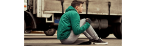 man in green hoodie and sweatpants with yoga mat next to semi truck