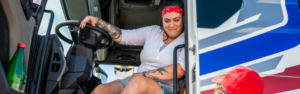 woman with tattoos sitting at the wheel in the cab of a semi truck with the door open