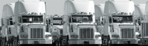 black and white photo of several semi trucks that are mostly the same make and model parked together in a group or fleet