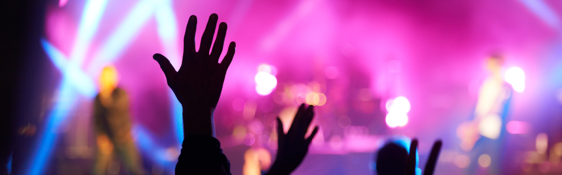 People raising their hands as a concert is going on and performers are on stage.
