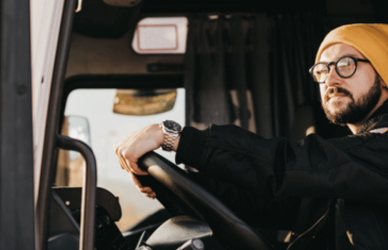 Young man with glasses and stocking hat at the wheel of a semi truck