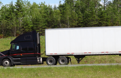 black semi truck with white trailer driving on road surrounded by green grass