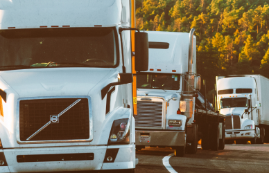 white volvo semi truck followed by other semi trucks