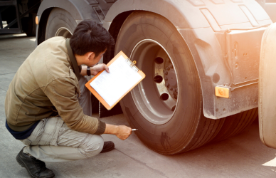 man with clipboard kneeling near semi truck tires