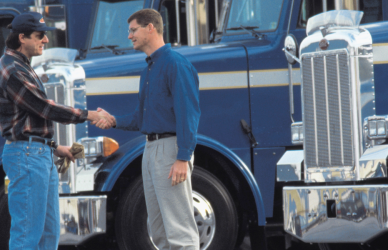two men shaking hands in front of semi trucks