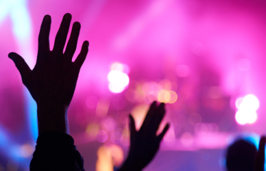 People raising their hands as a concert is going on and performers are on stage.