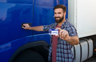 man standing next to semi truck holding up cdl