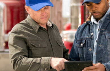 two men looking at tablet in front of semi truck