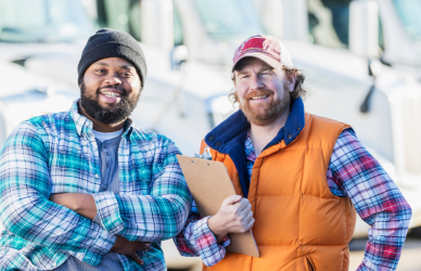 two smiling men standing in front of semi trucks