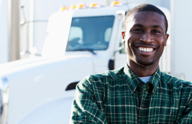 black man in flannel shirt standing in front of semi truck
