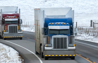 two older semi trucks driving on highway with snowy shoulders