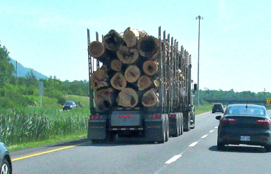logging semi truck passing car on four lane highway