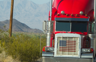red semi truck with american flag in grille on road