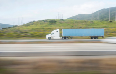 white semi truck with blue trailer on road with mountains in background