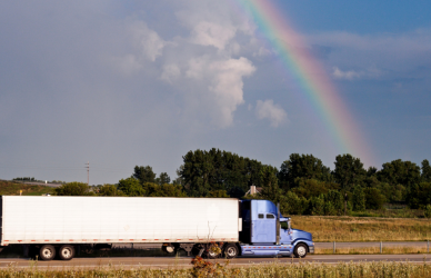 blue semi truck with white trailer driving on road with rainbow in background