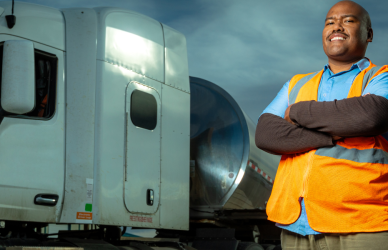 black man standing with crossed arms in front of white semi truck