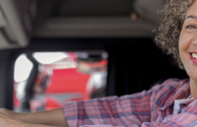 black woman in pick plaid shirt driving semi truck