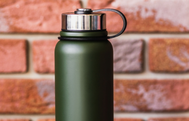 green insulated water bottle with brick wall in background