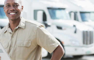 black man with tablet in front of white semi trucks