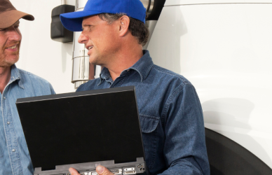 two men in hats looking at laptop with white semi truck in background