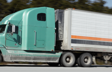 green truck pulling white trailer with orange and black stripes