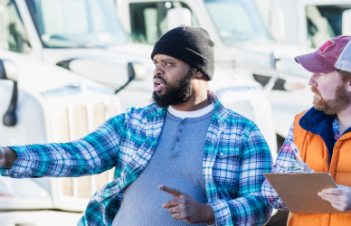 two men in front of a row of parked semi trucks