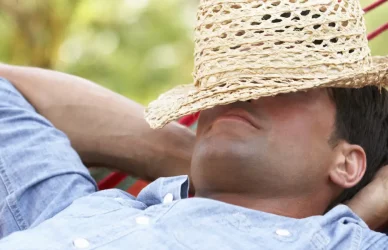 man relaxing in hammock with straw hat over face