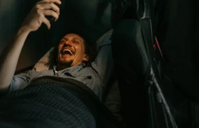 man in sleeper laughing as he looks at phone