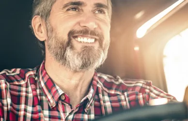 man with salt and pepper beard and hair behind the wheel of a semi truck