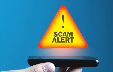 man holding phone with a scam alert icon hovering above it on a blue background