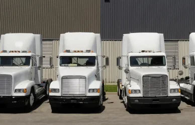 white semi trucks parked in a line in front of a metal building