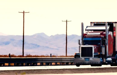 red semi truck with white trailer on bridge with mountains in background