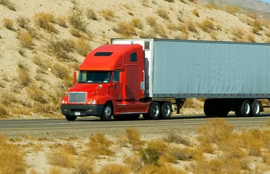 red semi truck pulling white trailer on desert road